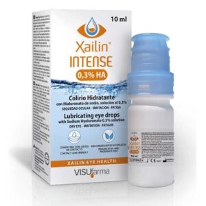 A product image featuring a box and bottle of Xailin Intense, 0.3% Sodium Hyaluronate eye drops. The box is predominantly white with blue accents, displaying the product name and concentration prominently at the front. It also includes additional information such as “Lubricating eye drops,” “Soothes,” “Hydrates,” and “Relieves fatigue.” The bottle has a blue cap and a clear body, allowing the liquid inside to be visible. The background includes an image of water splashing, symbolizing hydration.